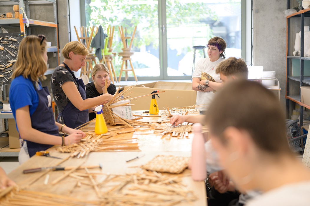 A group of students at a workbench are learning the craft of braiding